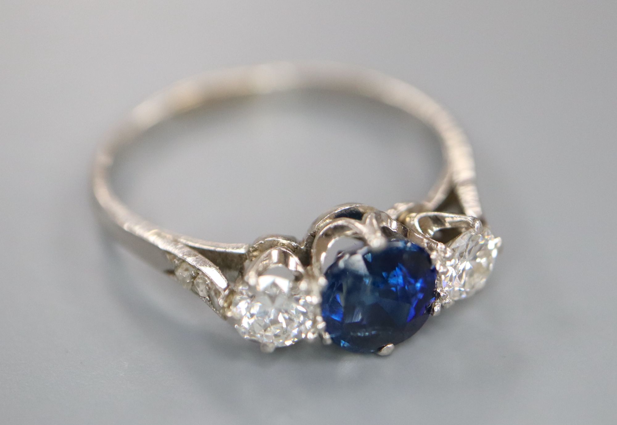 A white metal, sapphire and diamond three stone ring, with diamond chip set shoulders, size Q, gross 3.6 grams.